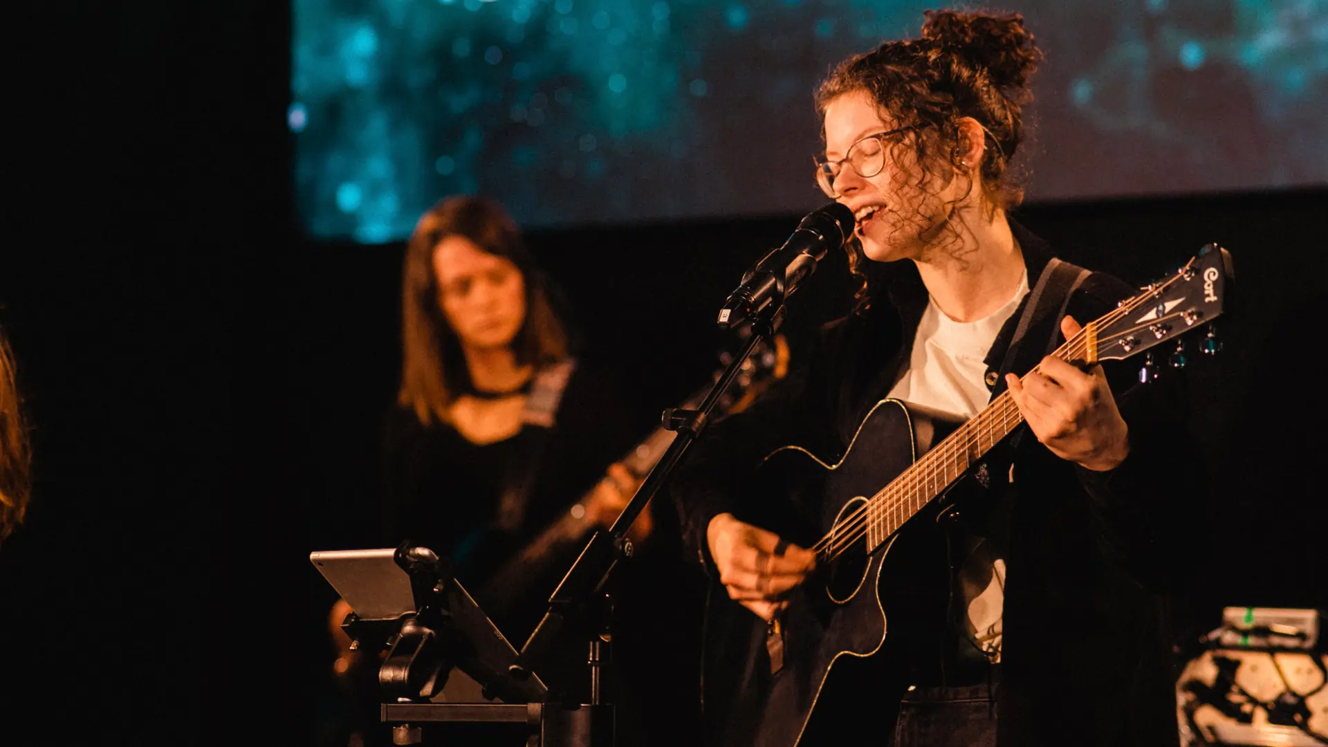 Eine Frau singt auf einer Bühne in ein Mikrofon und spielt Gitarre